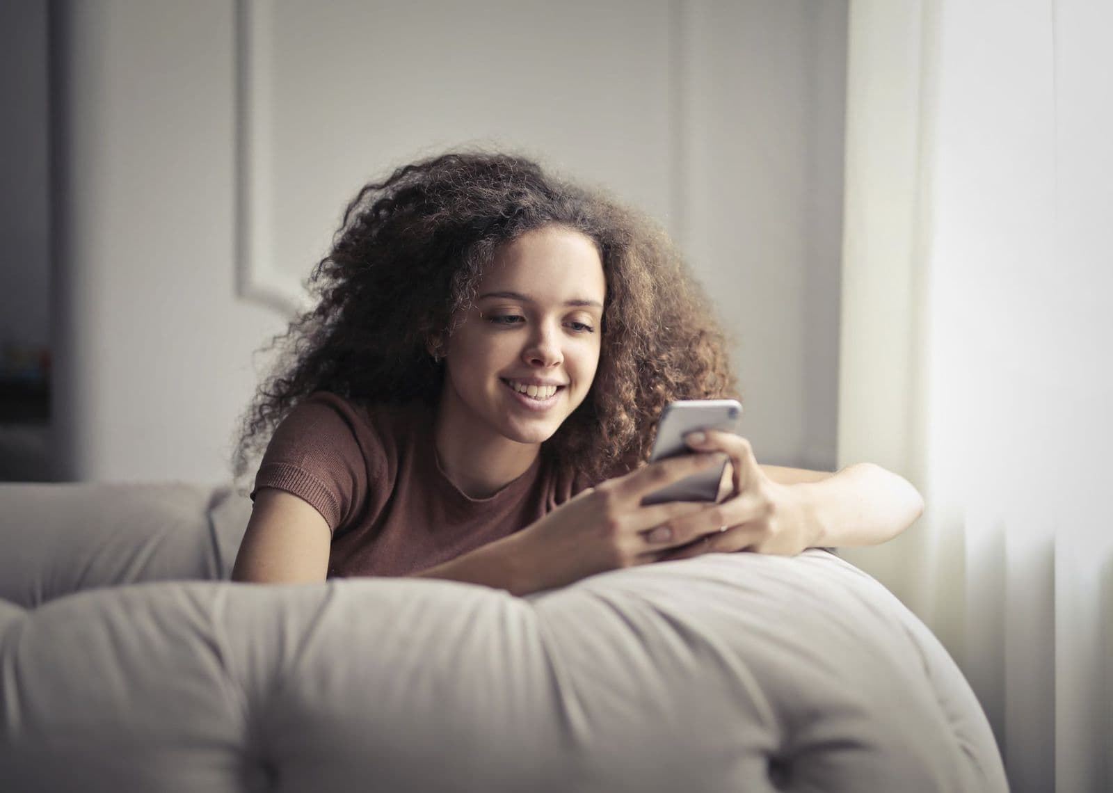 A smiling young woman booking an appointment on her phone at home