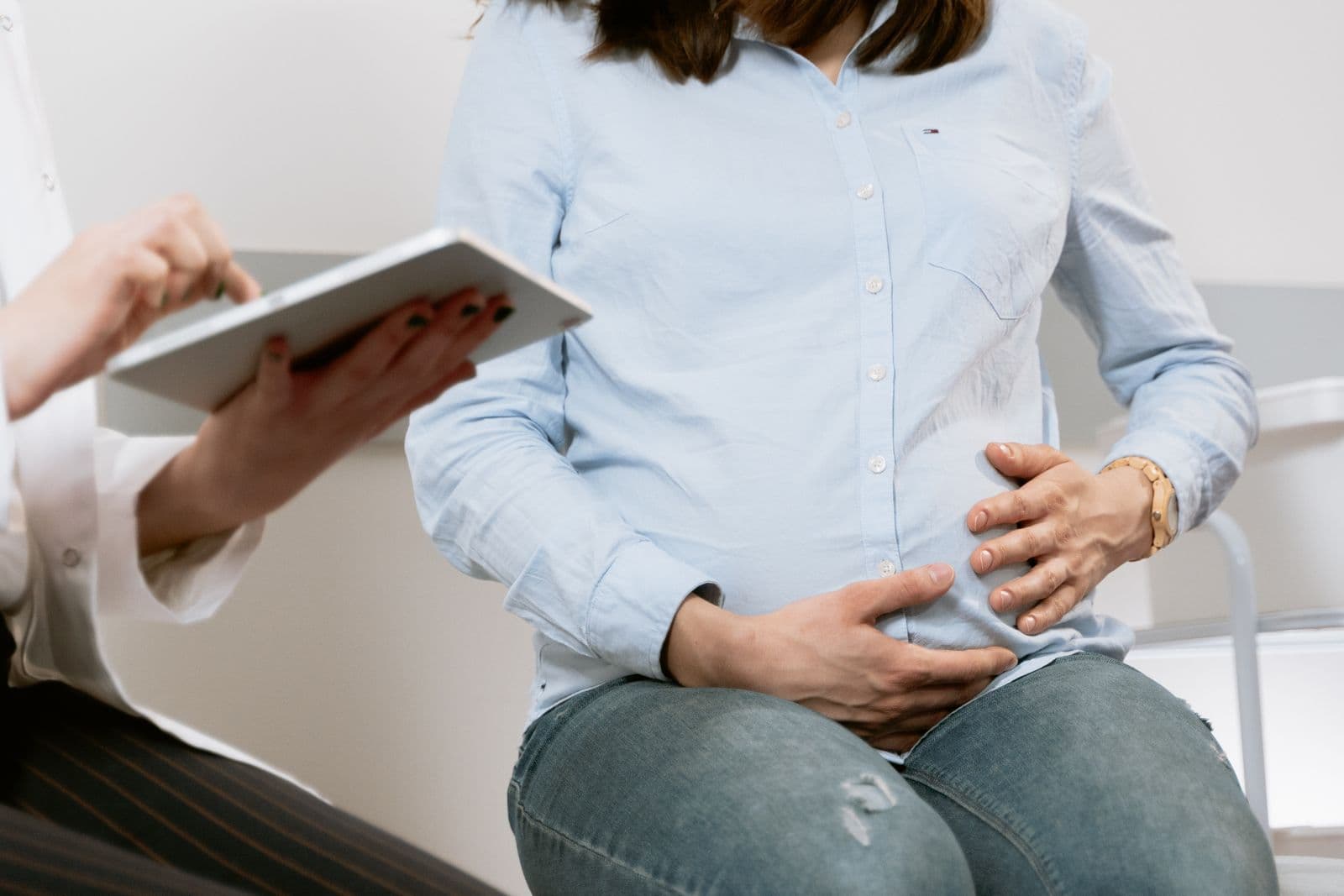 An expectant mother resting her hands on her belly while a clinician takes notes