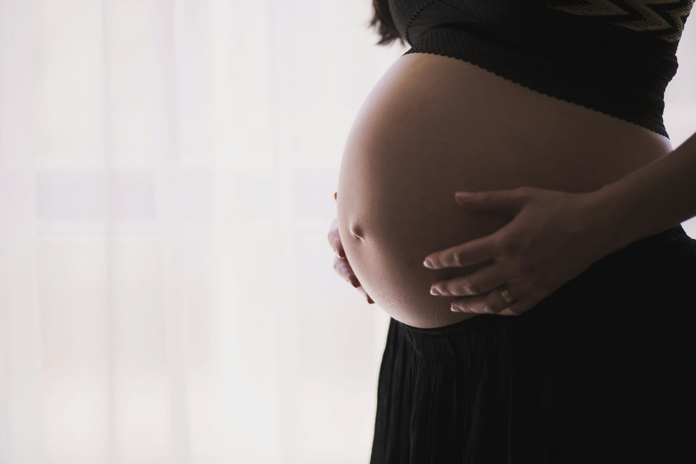 An expectant mother cradling her belly in soft window light